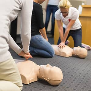 A group of adult education students practitcing CPR chest compressioon on a dummy.